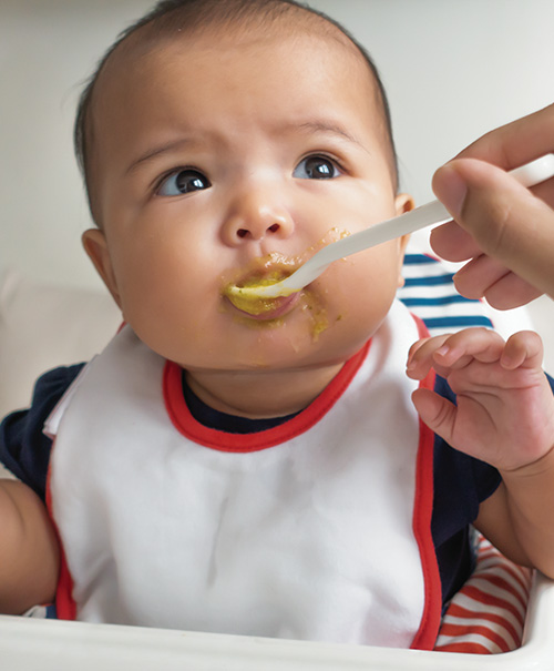 A baby spoon-fed pureed food, looking curious and engaged.