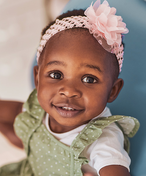 Smiling baby wearing a green polka dot dress and headband with a flower
