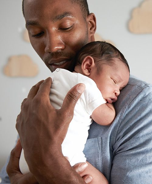Father holding a sleeping baby close to his chest in a nursery with cloud decorations