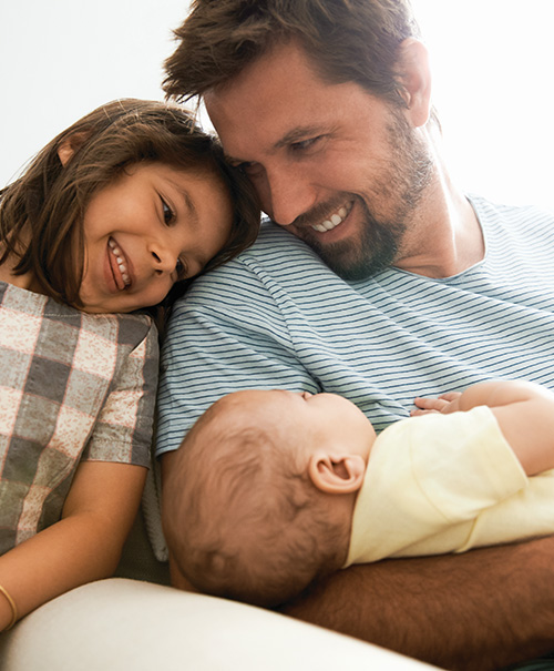 Father holding a baby while smiling at his young daughter sitting beside him