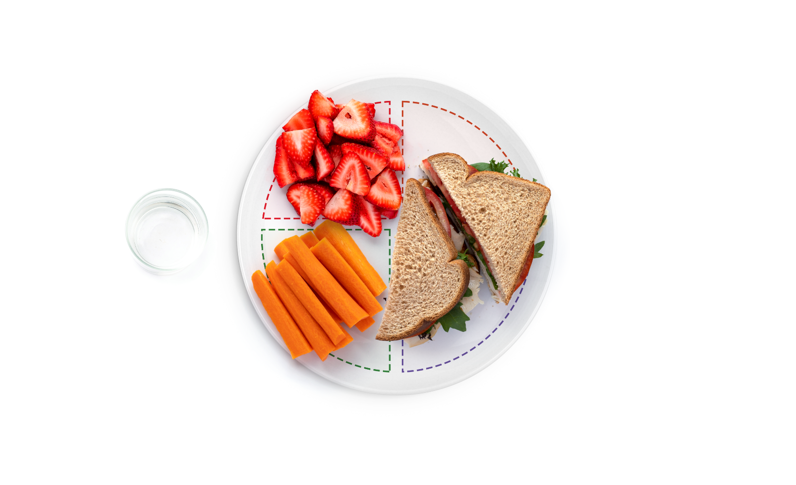 A healthy lunch plate featuring a sandwich, carrot sticks, and sliced strawberries, with a small glass of water on the side.